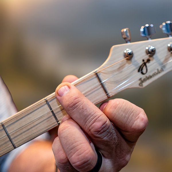 A hand fretting a chord on the maple neck of a Boondocker Trailhead
